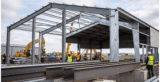 Montagem de uma estrutura metálica para galpão industrial com vigas de aço carbono e trabalhadores no canteiro de obras.